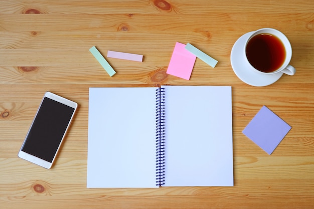 Las páginas vacías abrieron el cuaderno, el teléfono inteligente, el bloc de notas y una taza de té caliente en la mesa de trabajo de madera