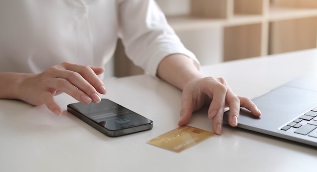 Pago en línea, manos de mujer sosteniendo teléfono inteligente y usando tarjeta de crédito para compras en línea.