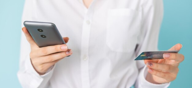 Pagos en línea Oficina mujer Servicio de crédito bancario Señora irreconocible camisa blanca clásica con tarjeta de plástico smartphone aislado repisa ancha azul