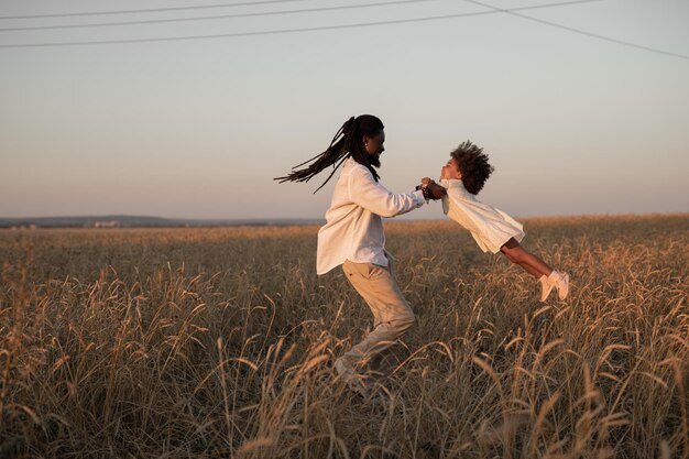 Foto pai africano feliz gira sua filha em seus braços em um campo