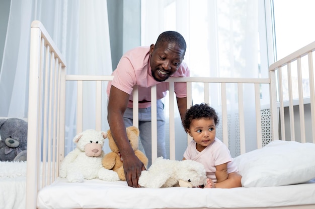 Pai afro-americano coloca filho bebê na cama em casa