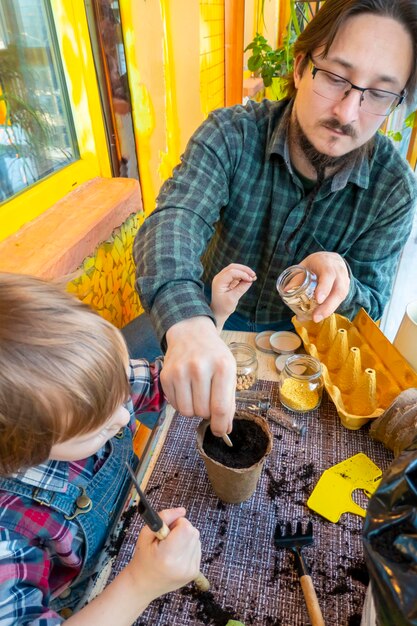 Pai ajuda seu filho a plantar sementes em um pote de turfa