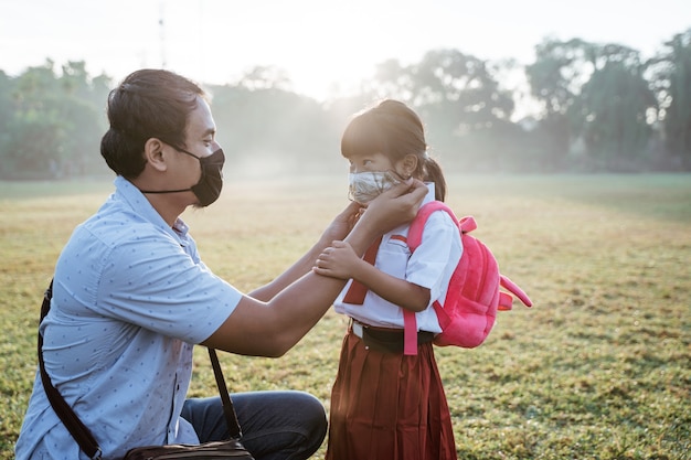 Pai ajudando a filha a usar uma máscara antes de ir para a escola