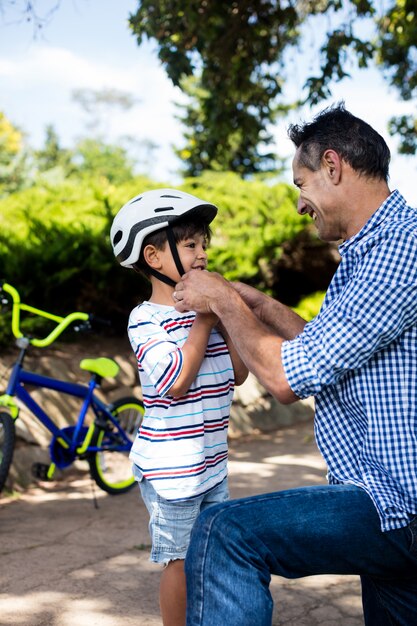 Pai, ajudando o filho a usar capacete de bicicleta no parque