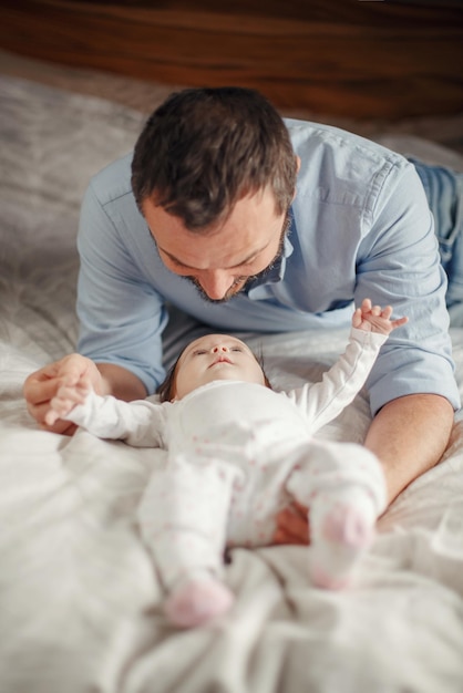 Pai alegre brincando com a filha enquanto deitado na cama em casa