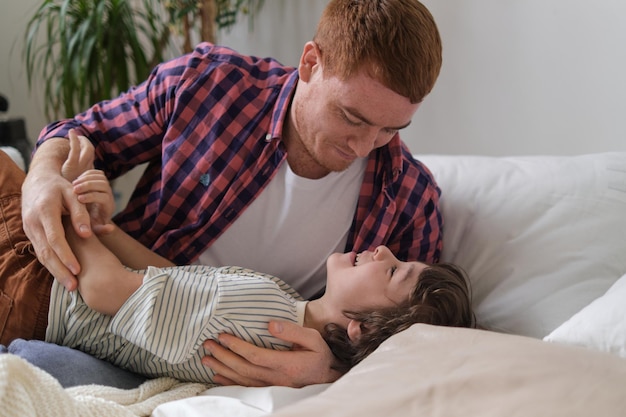 Pai alegre e filho se unindo por meio de cócegas divertidas, criando uma atmosfera calorosa e feliz no quarto