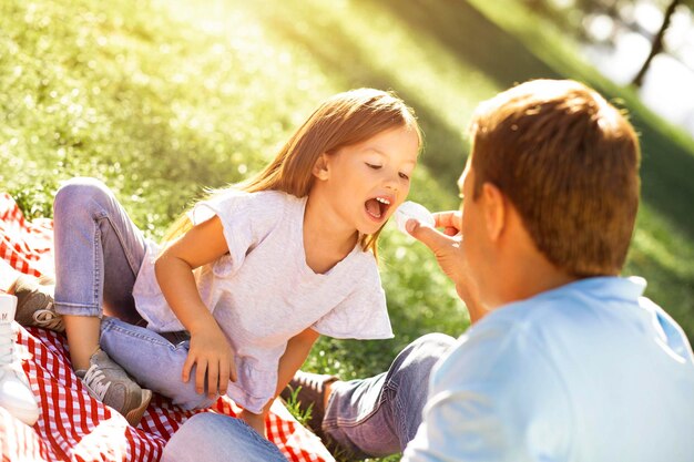 Pai alimentando a filha com marshmallow no piquenique no parque