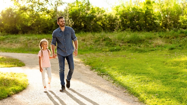 Pai andando com sua filha de mãos dadas e olhando de lado para a família de espaço livre curtindo um passeio