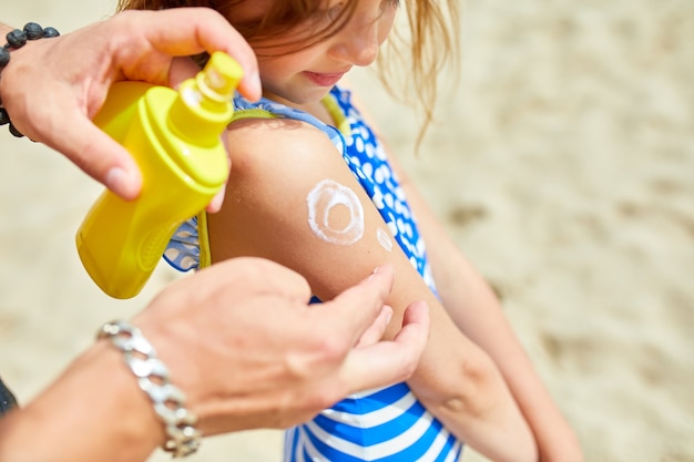 Pai aplicando protetor solar na filha na praia, Pai pintando protetor solar no ombro em forma de sol, protetor solar para a pele. Férias de verão.