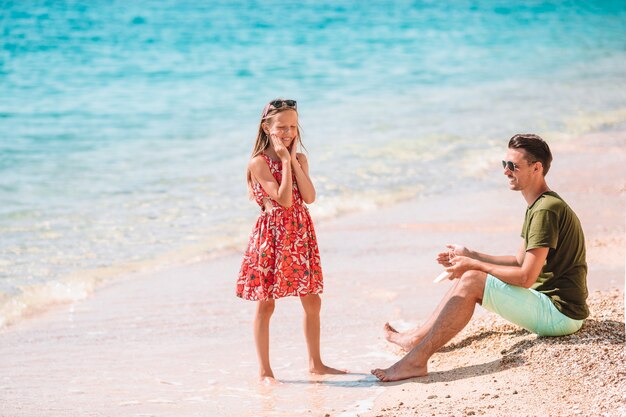 Pai, aplicar creme de proteção solar para sua filha na praia tropical