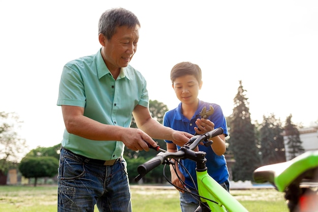Pai asiático ajudando filho a consertar bicicleta com ferramentas garotinho coreano assistindo o pai consertar bicicleta quebrada