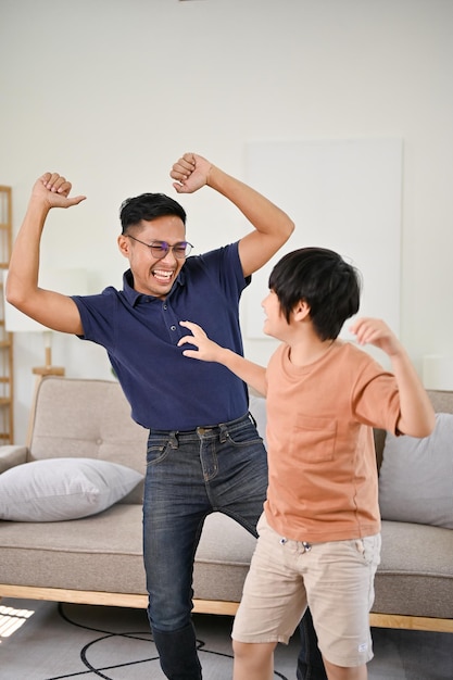 Pai asiático alegre e brincalhão e filho pequeno gostando de dançar juntos na sala de estar