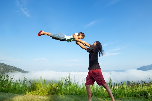 Pai asiático carregando sua filha no ar e brincando juntos na bela névoa e montanha com diversão e amor