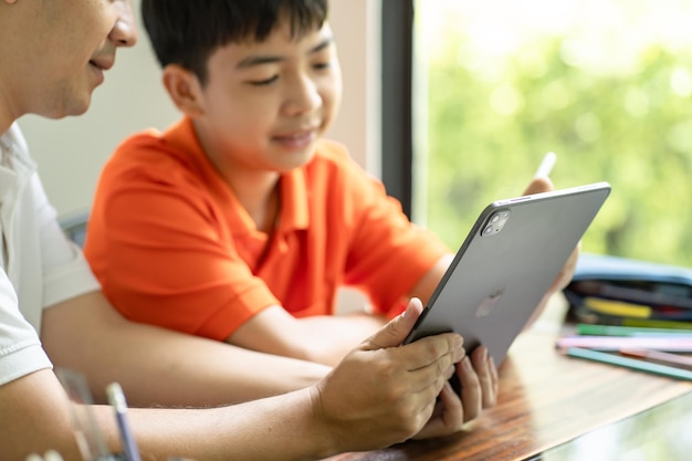 Pai asiático e filho usando tablet ensinando filho a desenhar xAplaying com tablet digital na paternidade de mesa