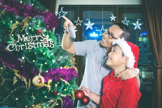 Pai asiático e seu filho olhando para uma árvore de Natal