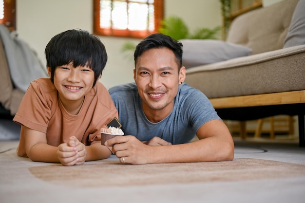 Pai asiático feliz e sorridente e filho deitado no chão da sala juntos