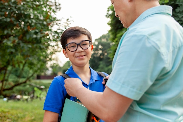 Pai asiático velho vai para a escola com o filho e carregar livros menino coreano com mochila e óculos