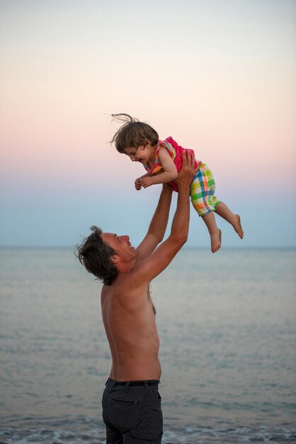 Pai brincando com filha fofa enquanto está de pé contra o mar na praia