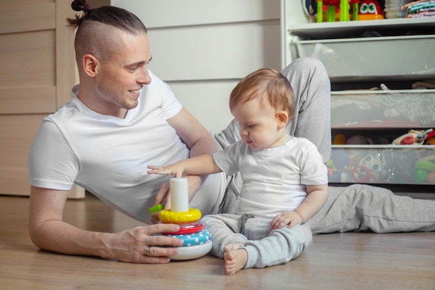 Pai brincando com seu filho bebê com um brinquedo de pirâmide no quarto das crianças