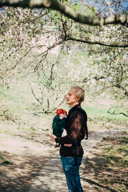 Pai caminhando com a filha bebê no jardim, usando mochila tipo sling