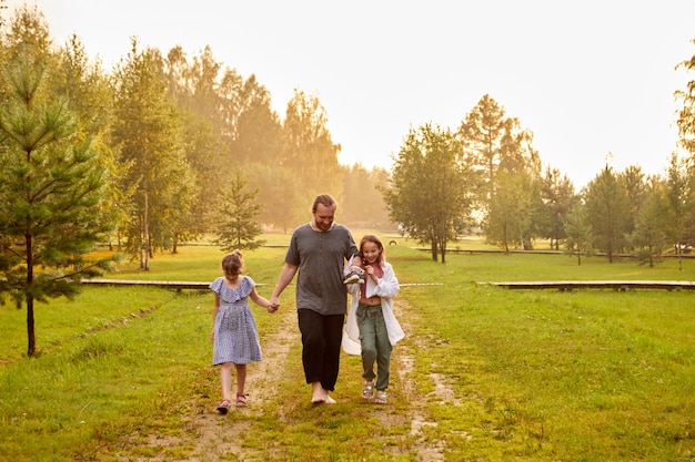 Pai caminhando com as filhas no campo ao pôr do sol