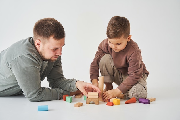 Pai carinhoso brinca com filho alegre com cubos de madeira de brinquedo em fundo branco Paternidade e cuidados infantis