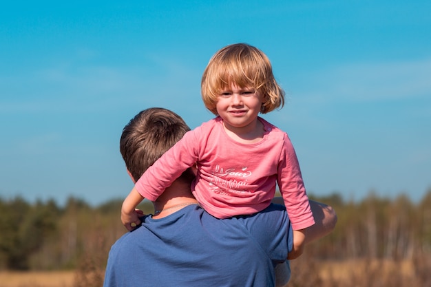 Pai carrega a filha nos braços no campo de verão com grama seca