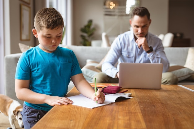 Pai caucasiano usando laptop enquanto filho fazendo sua lição de casa em casa