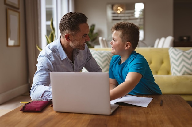 Pai caucasiano usando laptop para ajudar seu filho com a lição de casa em casa
