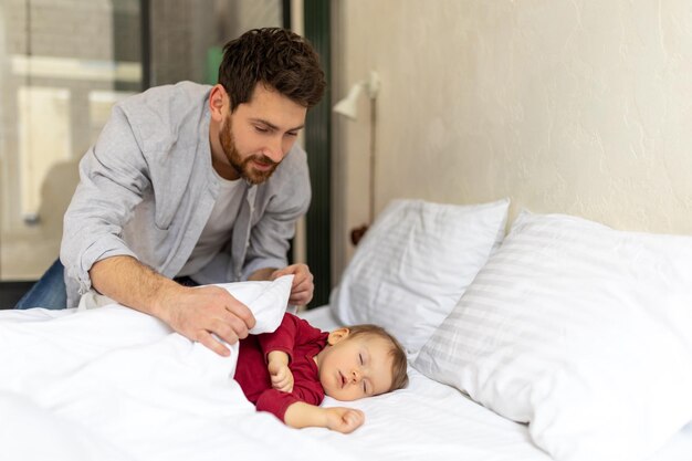 Pai cobrindo seu bebê adormecido com um cobertor em casa