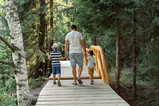 Pai com dois filhos caminhando no parque em um caminho de madeira