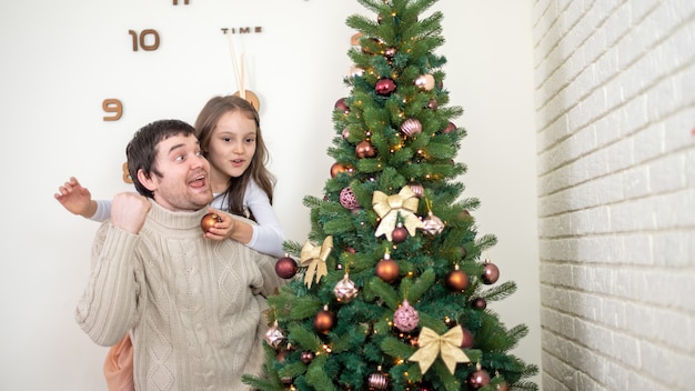 Pai com filha está decorando a árvore de natal em casa. ideia de família feliz