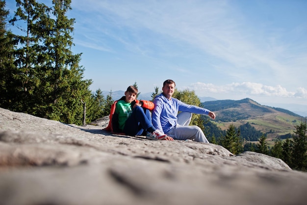 Pai com filho crianças caminhando em um lindo dia nas montanhas descansando na rocha e admirando a vista incrível para os picos das montanhas lazer ativo de férias em família com crianças diversão ao ar livre e atividade saudável