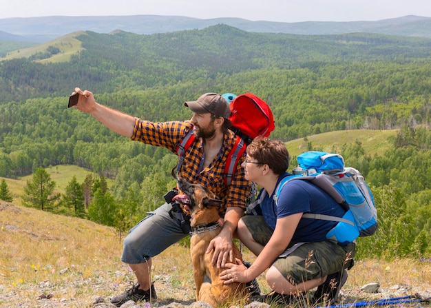 Pai com filho e seu cachorro tiram uma selfie no topo da montanha