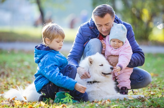 Pai com filho pré-escolar e filha brincando com cachorro samoiedo no parque outono