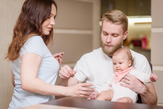 Pai com mãe alimentando sua filha com purê de frutas na cozinha