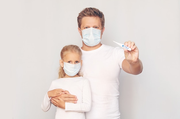 Pai com máscara médica mede a temperatura da filha com um termômetro eletrônico em um fundo isolado