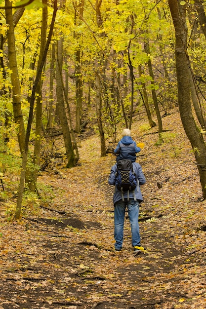 Pai com o filho nos ombros, caminhando na floresta de outono.
