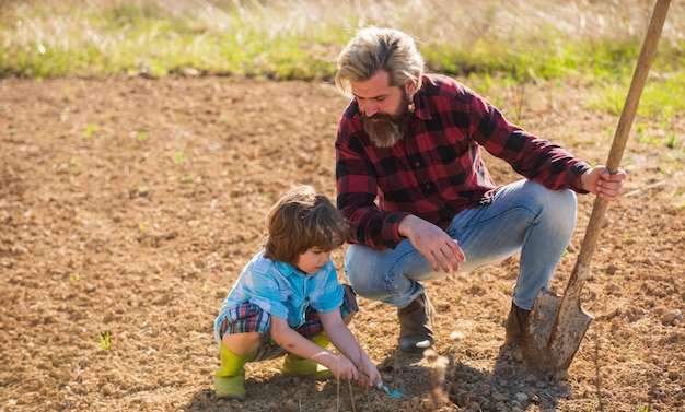 Pai com pá e menino cavando o solo De onde vem a comida Ensinando o filho a cultivar plantas Plantando plantas Trabalha no campo Pai agricultor instrui o bebê como plantar Agricultura ecológica Habilidades reais