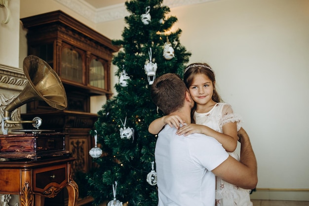 Pai com presente abraçando sua filha perto da árvore de Natal em casa