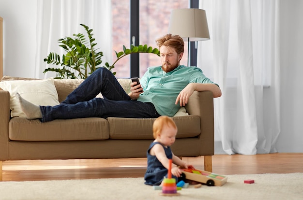 pai com smartphone e bebê brincando em casa