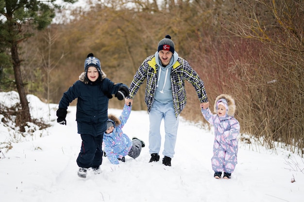 Pai com três filhos de mãos dadas e caminhando na floresta de inverno