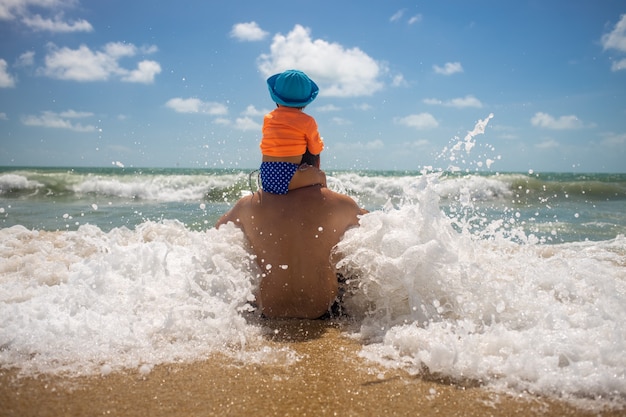 Pai com um bebê nos ombros brincando com o spray de espuma do mar conceito de infância feliz