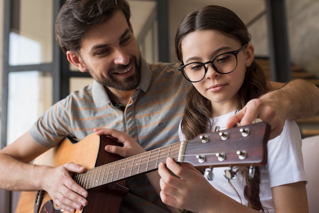 Foto pai de ângulo baixo, ensinando a menina a tocar violão