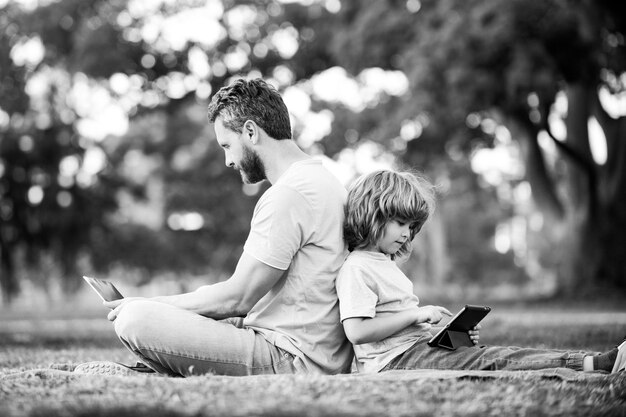 Pai de aprendizagem à distância ao ar livre usando laptop relaxa com filho escolar segurando laptop se diverte juntos