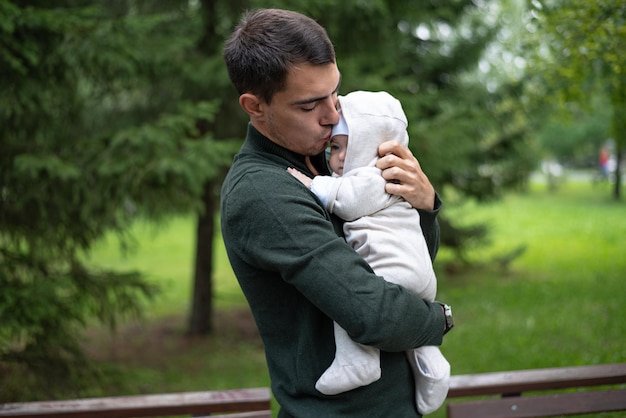 Pai de cabelo escuro na jaqueta verde beija seu bebê infantil nas mãos feliz paternidade amor incondicional