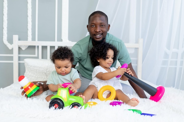 Pai de família afro-americano com filhos, bebês, brincam e colecionam uma pirâmide colorida em casa na cama, família feliz