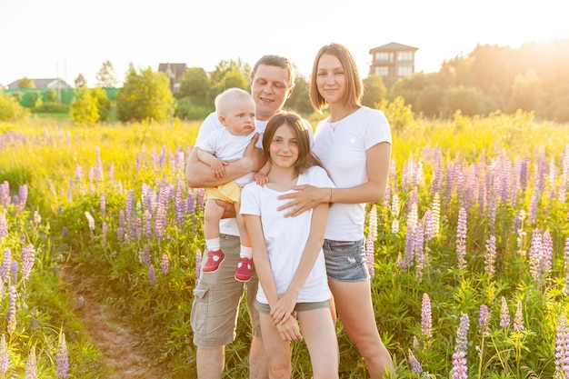 Pai de mãe de família feliz abraçando crianças ao ar livre. Mulher homem bebê filho e adolescente no campo de verão com fundo de flores desabrochando. Família feliz, mãe, pai e filhas brincando no Prado.