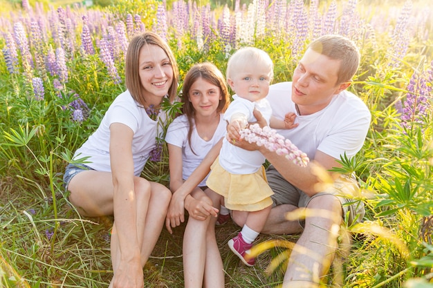 Pai de mãe de família feliz abraçando crianças ao ar livre. Mulher homem bebê filho e adolescente sentada no campo de verão com fundo de flores desabrochando. Família feliz, mãe, pai e filhas brincando no Prado.