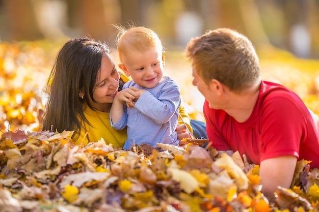 Pai de mãe de família feliz e bebê no parque outono, brincando com folhas.